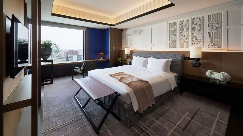 Modern, elegant hotel suite with floor-to-ceiling windows, plush king bed, contemporary furnishings, and city views of Kanazawa, Japan