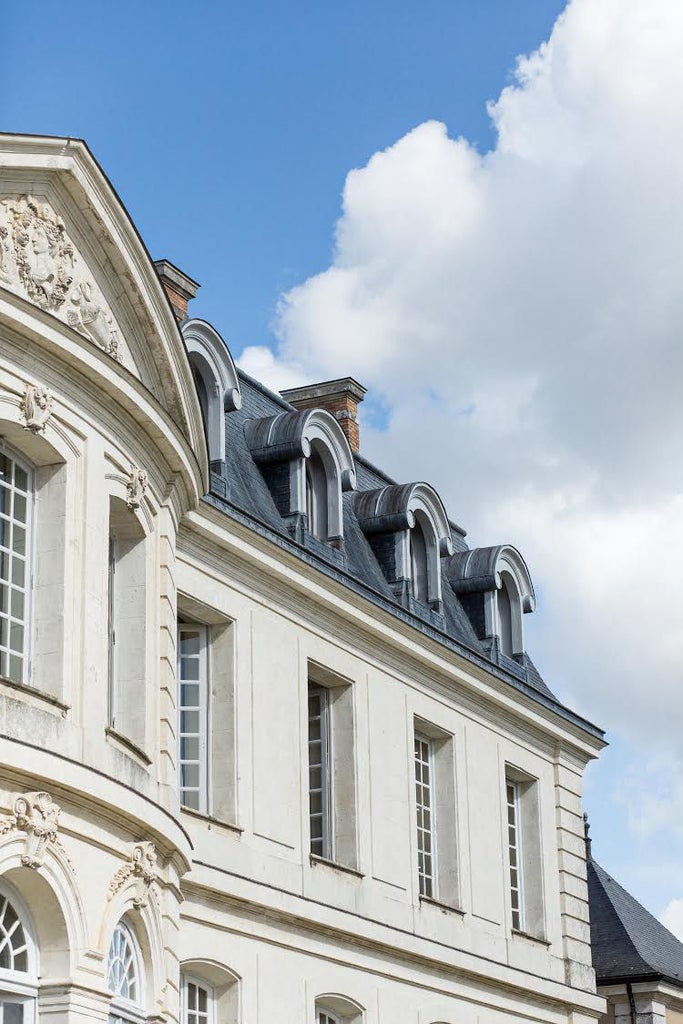 Elegant 18th-century French château hotel with symmetrical architecture, manicured gardens, and pale yellow limestone facade at golden hour