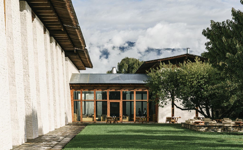 Serene mountain lodge with traditional Bhutanese architecture surrounded by pine forest and snow-capped peaks at golden hour