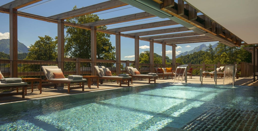 Modern alpine wellness resort nestled in Swiss mountains with glass facade, infinity pool overlooking Lake Lucerne and snow peaks