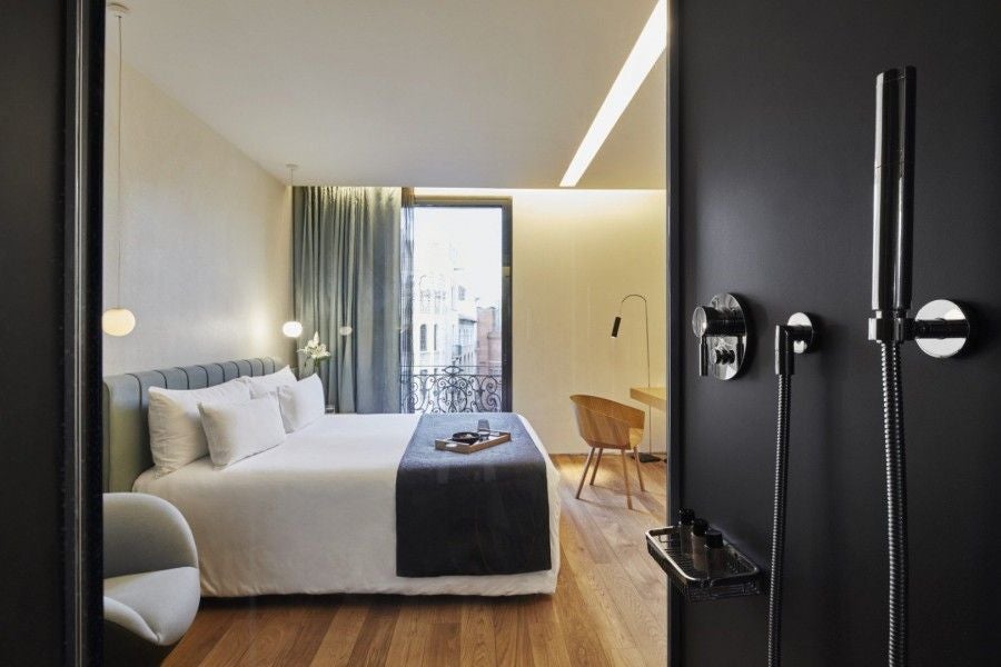 Minimalist luxury hotel room with sleek white walls, modern furniture, and large window offering soft natural light in Barcelona's stylish urban hotel