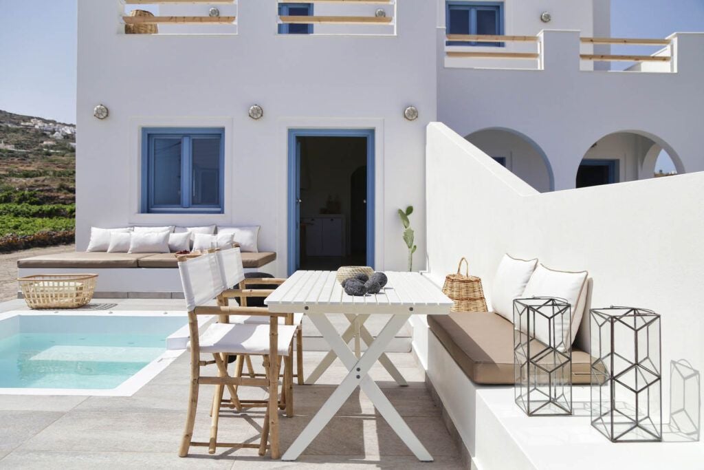 Luxurious white-washed Greek villa with blue-domed roofs overlooking the stunning Aegean Sea, nestled in the picturesque landscape of a traditional Santorini village