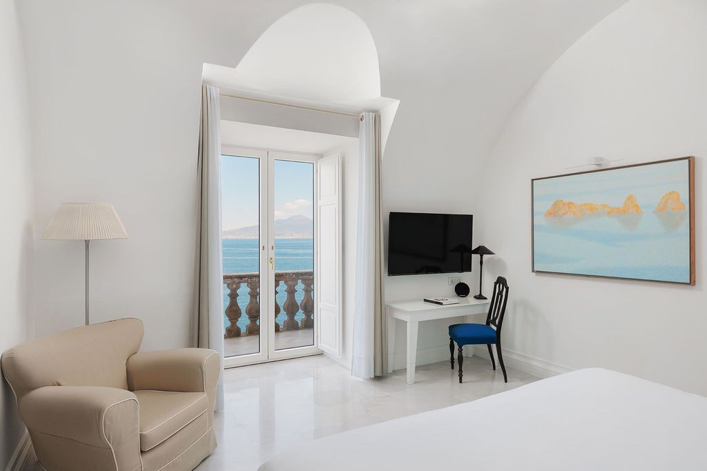 Elegant Italian suite with panoramic Mediterranean views, ornate chandeliers, plush white bedding, and refined coastal design in soft neutral tones