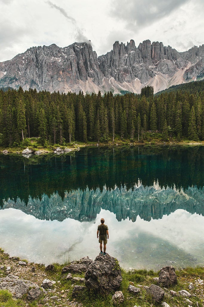 Majestic snow-capped Dolomites mountain peaks rise above a lush green valley at sunset, with pristine alpine lakes nestled below