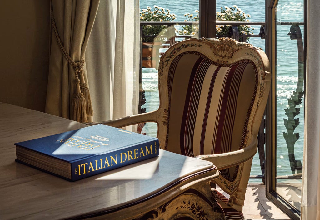 Opulent Venetian hotel suite with ornate furnishings, featuring a gilded king bed, antique mirrors, and lagoon views through arched windows