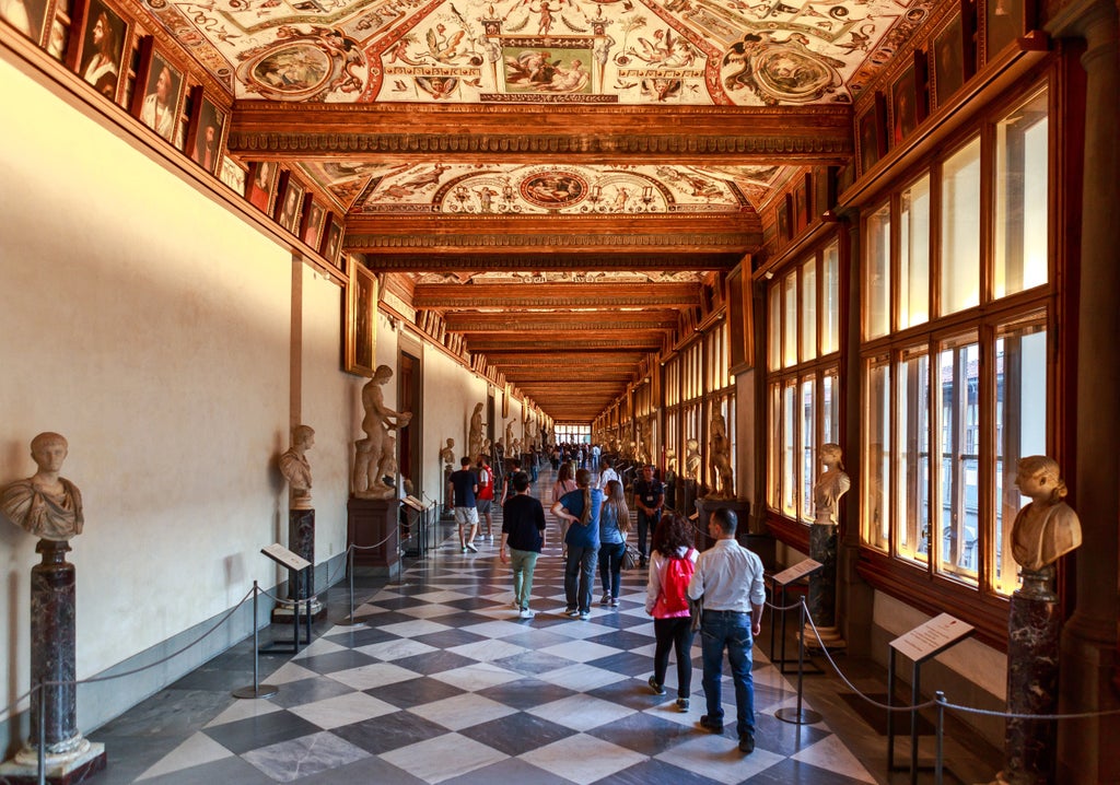 Grand corridor of Uffizi Gallery with ornate ceiling frescoes, marble statues, and Renaissance paintings illuminated by natural light