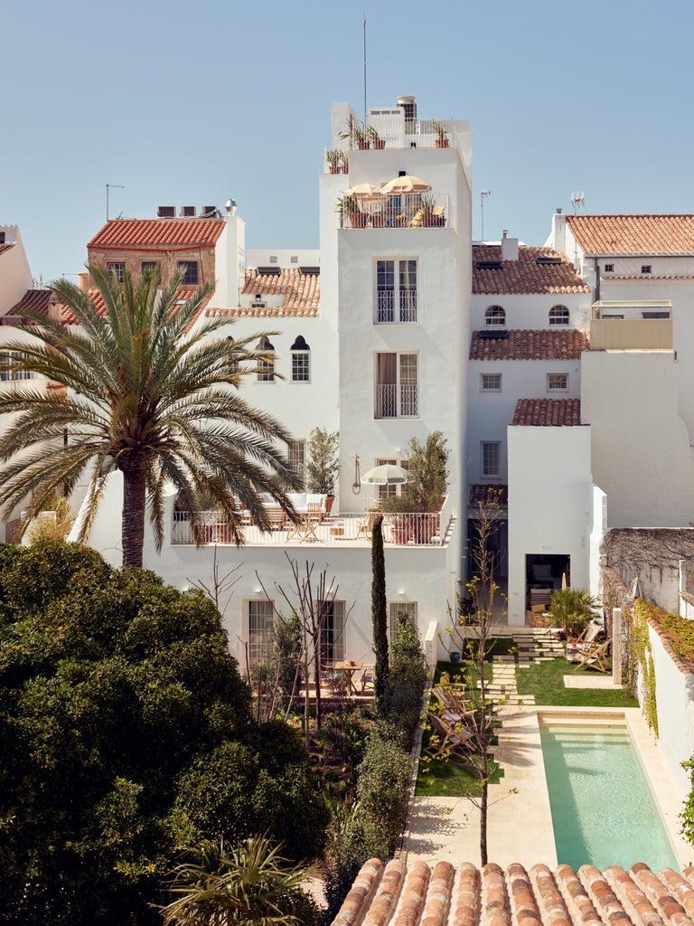 Elegant Spanish boutique hotel exterior with ivy-covered white facade, ornate balconies, and traditional wooden shutters at golden hour