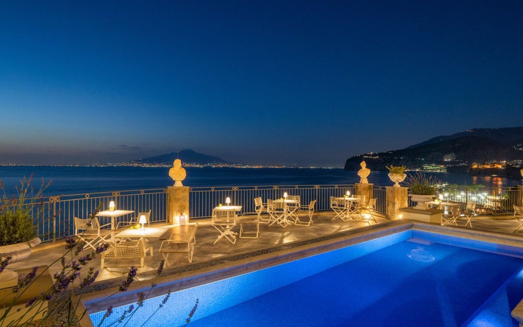 Luxurious coastal hotel with elegant stone facade overlooking the azure Mediterranean, perched on rocky cliffs of Sorrento with classic Italian architectural details