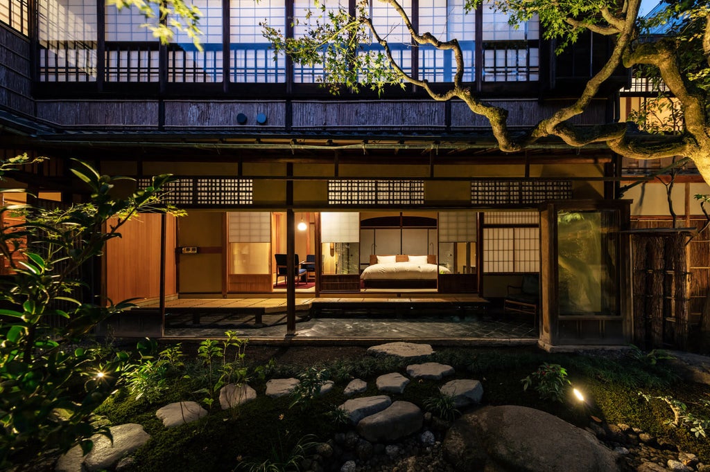 Traditional Japanese luxury hotel entrance with stone pathway, wooden gates, bamboo fencing and elegant lantern lighting at dusk