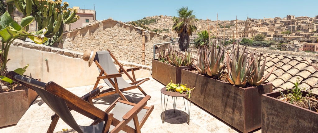 Rustic-chic hotel room in Sicilian stone house, featuring exposed wooden beams, minimalist decor, and warm terracotta tile flooring near Modica