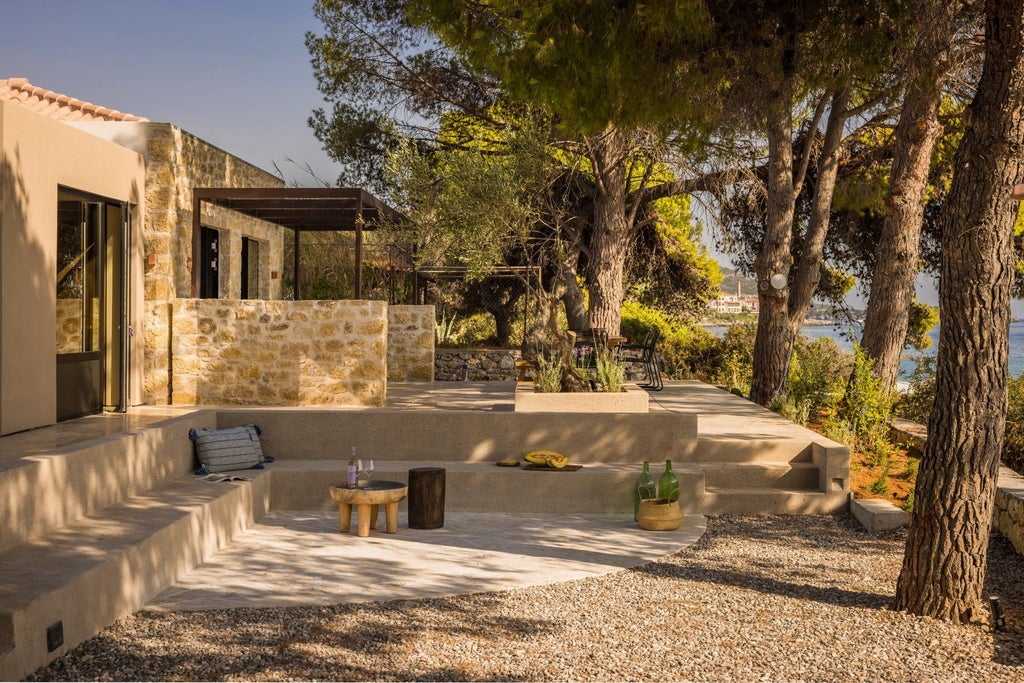 Serene stone villa with terracotta roof overlooking azure Aegean waters, surrounded by lush Mediterranean gardens at a luxurious Greek coastal retreat