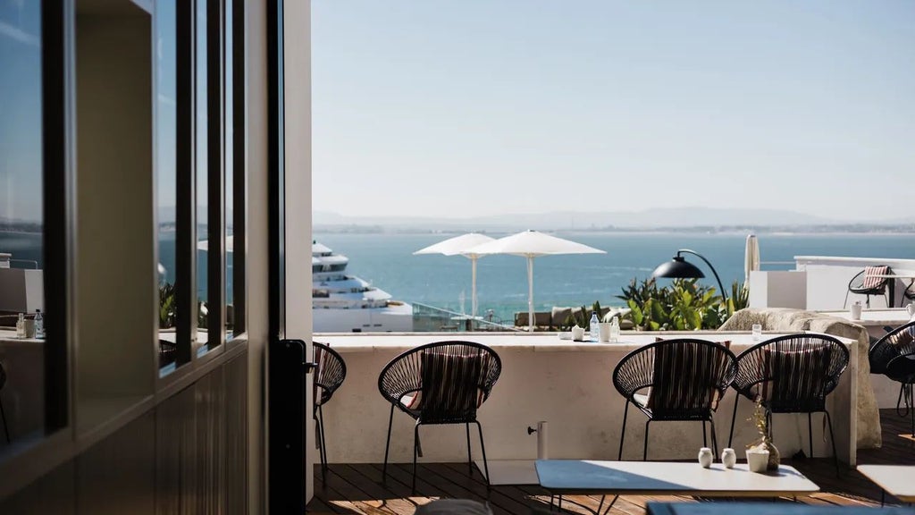 Boutique Hotel Memmo Alfama overlooking Lisbon's historic district, featuring elegant white terrace with vibrant red lounge chairs and panoramic city views