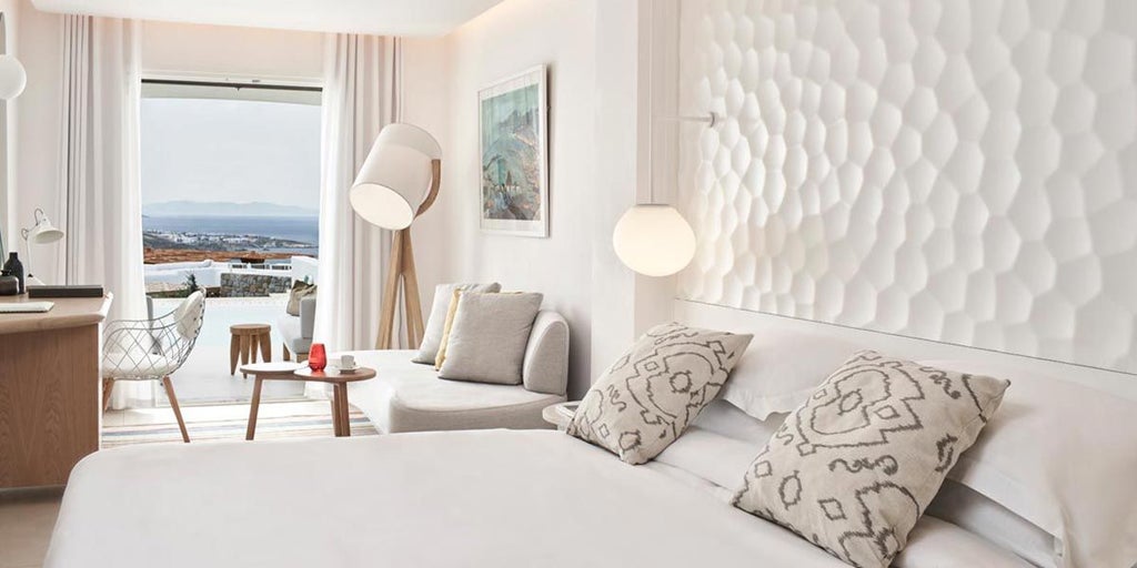 Luxurious white-washed Cycladic superior room with expansive Aegean Sea view, minimalist design, private balcony, and elegant modern furnishings in Mykonos