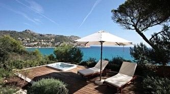 Luxurious Mediterranean coastal hotel perched on rocky cliffs near Cala Ratjada, Mallorca, with elegant white architecture and stunning blue sea view