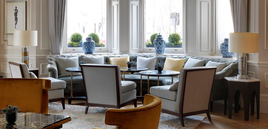 Luxurious exterior of a grand hotel in London, featuring elegant Georgian architecture with cream-colored facade and black wrought-iron details.