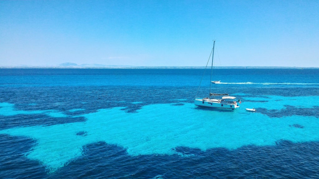 Luxury sailboat gliding through turquoise Aegean waters, passing sun-drenched Greek islands of Koufonissia and Schoinoussa with pristine coastlines