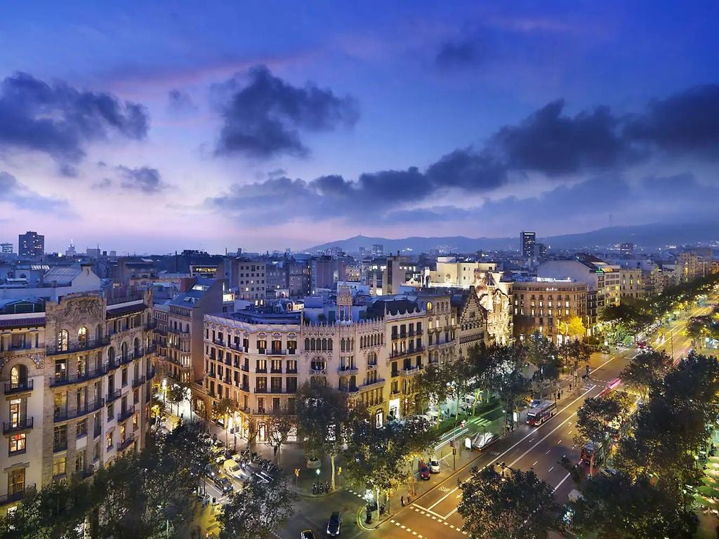 Elegant facade of Mandarin Oriental Barcelona hotel featuring sleek glass windows, ornate stone columns and sophisticated lighting at dusk