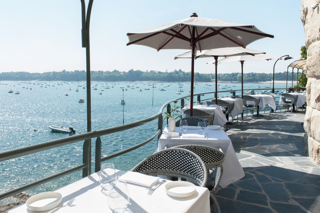 Elegant seaside hotel with blue-gray facade, nestled on rocky coastline, featuring pristine white balconies and panoramic ocean views in Brittany, France