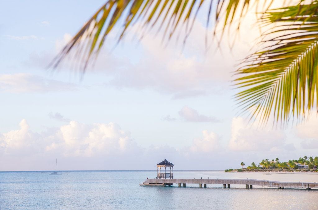 Luxurious beachfront resort with white sand, turquoise waters, palm trees, and elegant Caribbean-style villas at Scenset Bay Island in Antigua.