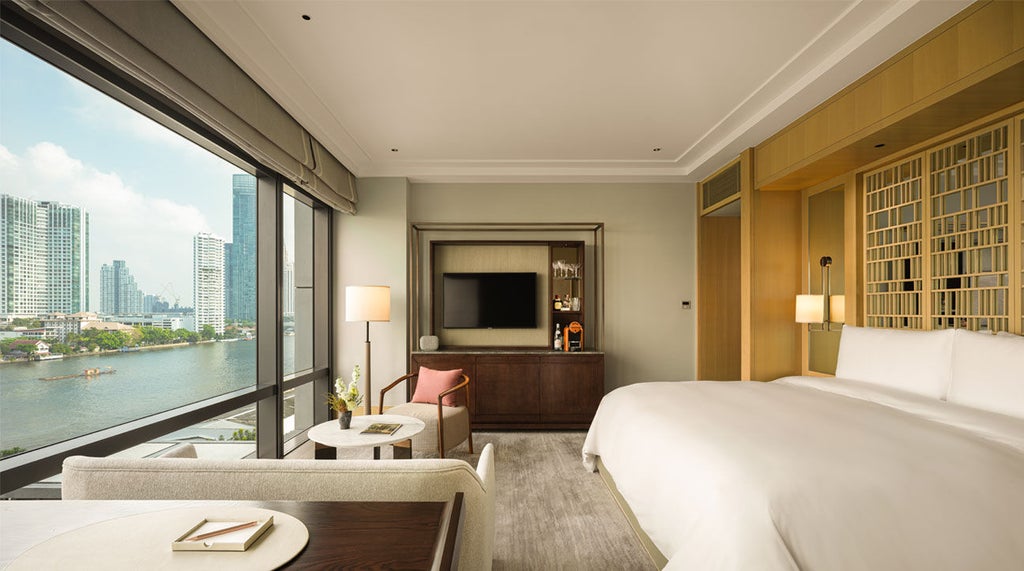 Elegant hotel room with floor-to-ceiling windows overlooking Bangkok river, featuring king bed, marble bath, and modern Thai decor