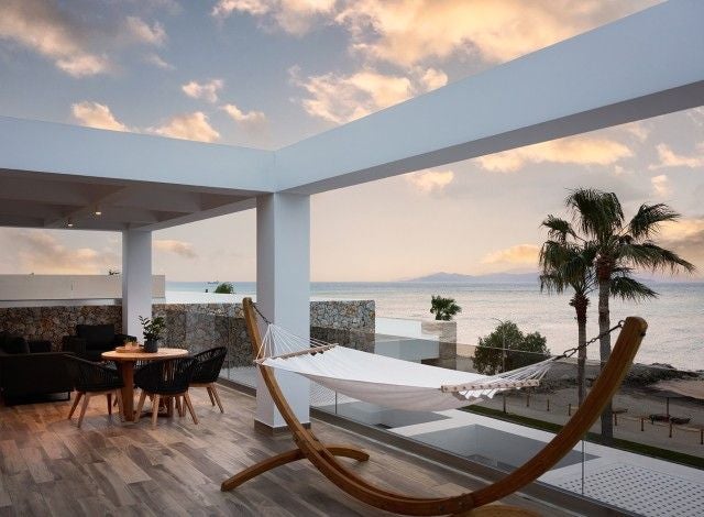 Luxurious master suite overlooking Aegean Sea, featuring modern minimalist design, private jacuzzi, and expansive floor-to-ceiling windows with panoramic coastal scenery