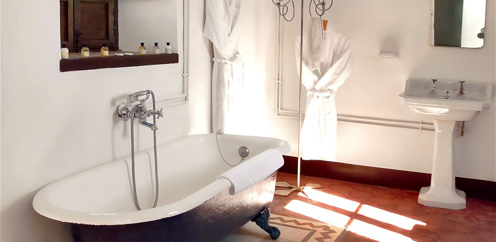 Rustic stone-walled Spanish hotel room with elegant wooden furnishings, arched windows, and soft lighting in a historic marqués estate