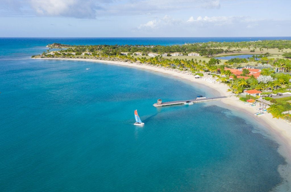 Pristine white sandy beach with turquoise waters, luxurious resort villas nestled among palm trees on a secluded Antiguan island paradise.