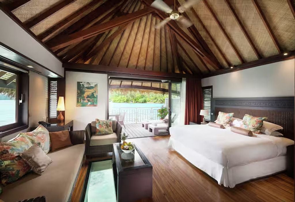 Luxurious overwater bungalow with glass floor panel, king bed, modern furnishings and panoramic views of Moorea's turquoise lagoon