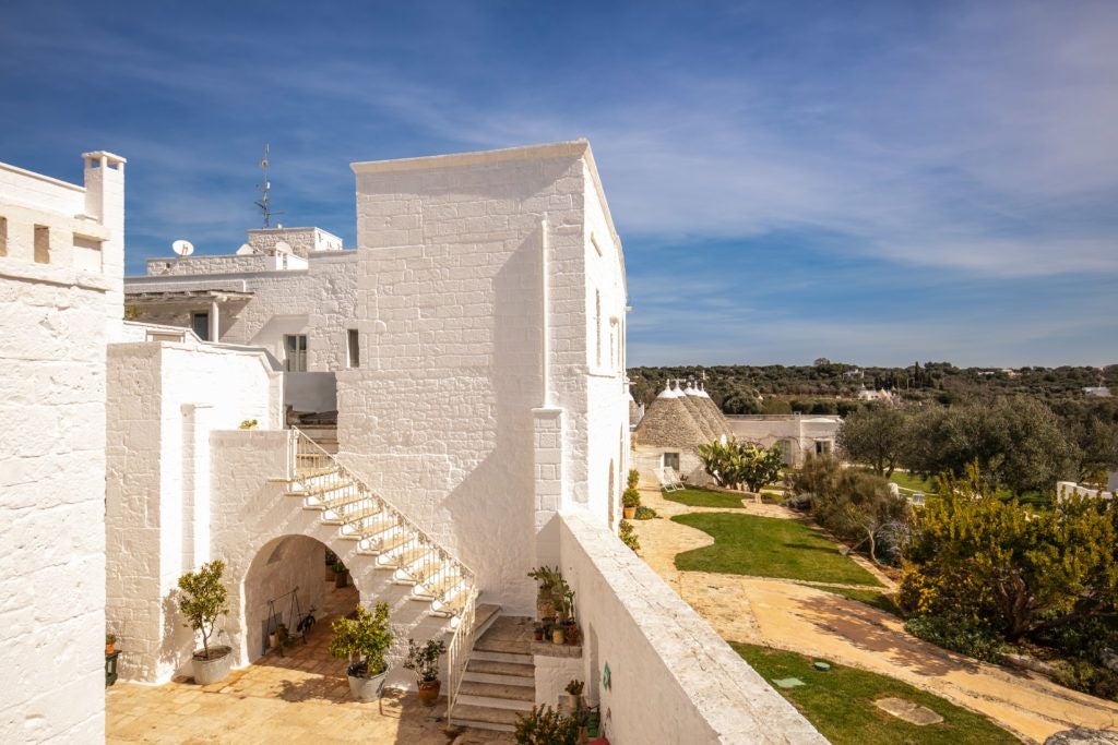 Rustic stone farmhouse with white-washed walls, surrounded by olive trees in Puglia, Italy, with warm evening sunlight casting golden hues across the landscape