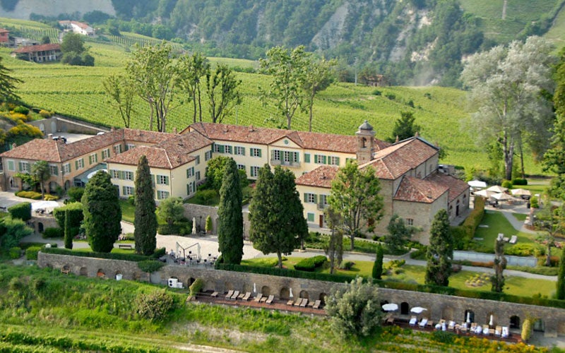 Elegant stone villa surrounded by manicured gardens and cypress trees, overlooking rolling hills of Italian countryside at golden hour