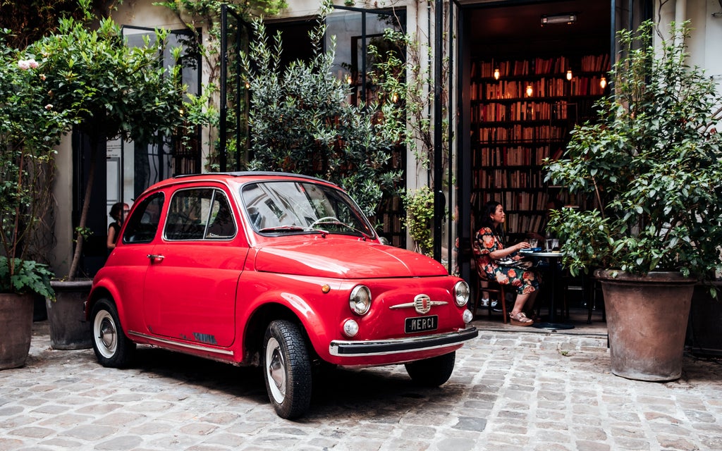 Colorful vintage Fiat 500s parked in line on a charming Italian street with rustic stone buildings and blooming flowers in window boxes