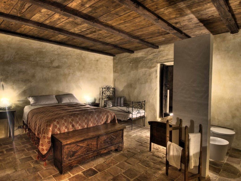 Rustic stone room with arched ceiling, handcrafted wooden bed, and warm terracotta tones in a traditional Italian mountain hotel suite