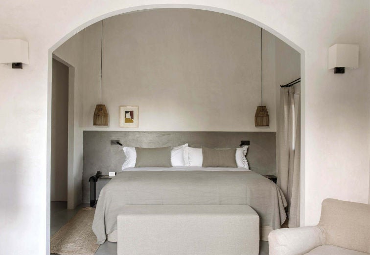 Contemporary hotel room with garden views, featuring rustic wood beams, beige textiles, and minimalist Mediterranean decor in neutral tones.