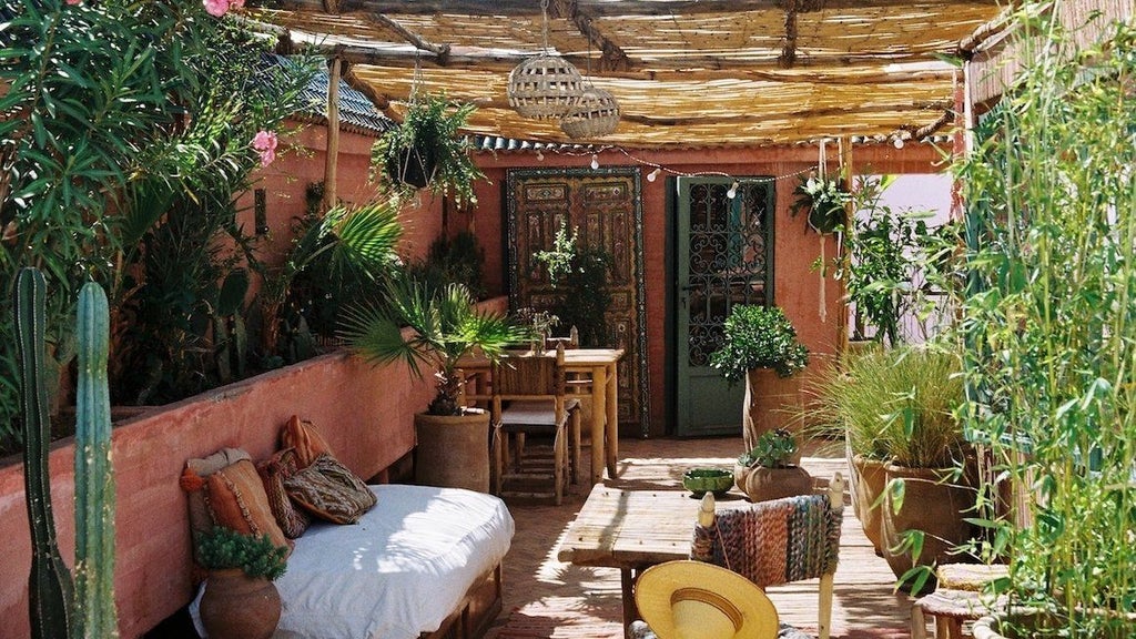 Pink-walled luxury riad courtyard with traditional Moroccan tilework, lush palms, and ornate archways surrounding a tranquil fountain