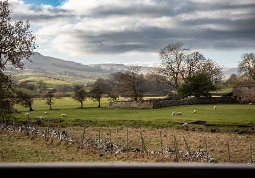 Elegant boutique hotel room with plush white bedding, modern minimal decor, large windows overlooking scenic countryside in scenic Yorkshire Dales region