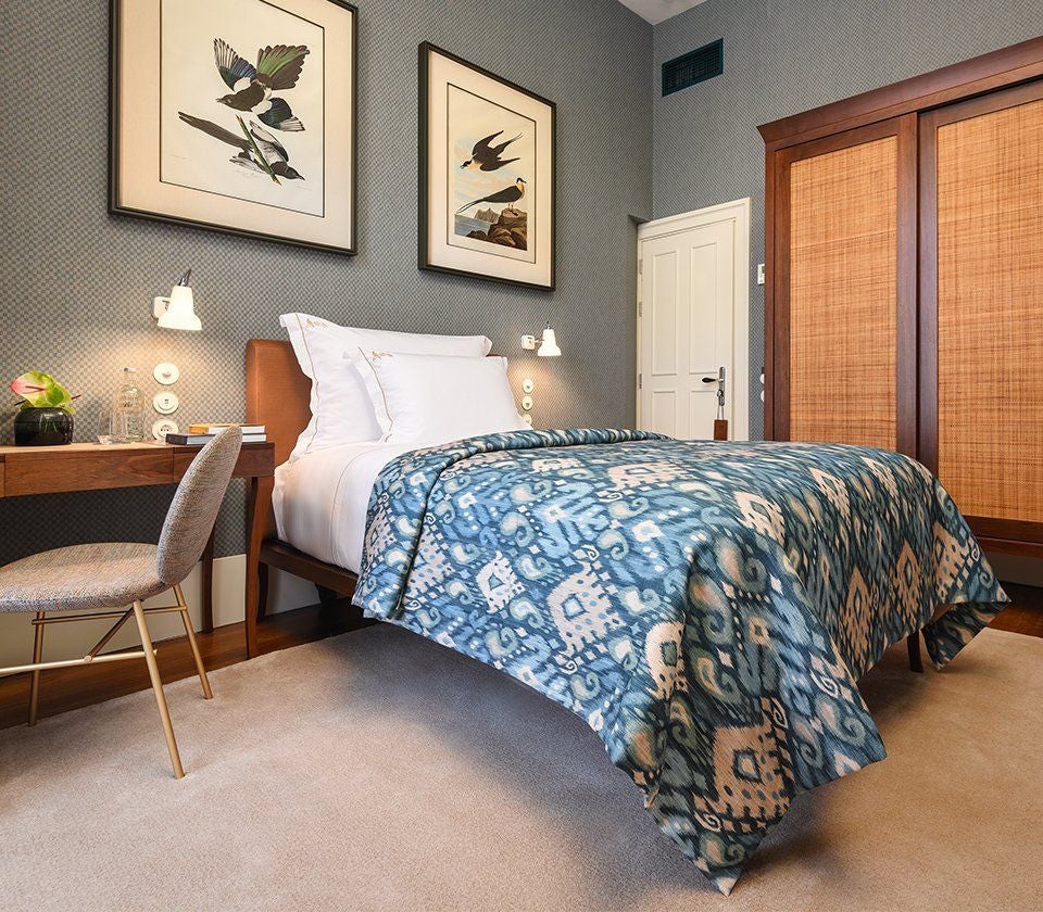 Single hotel room with elegant wooden bed, crisp white linens, vintage-style furnishings, and natural light streaming through tall windows