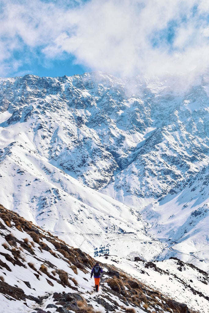 Luxurious hiking trail in Atlas Mountains with rugged terrain, distant Berber village, golden sunlight casting dramatic shadows on rocky landscape