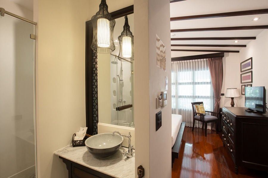 Elegant Lanna-style hotel room with ornate wooden furniture, draped mosquito net canopy over king bed, and traditional Thai decor elements