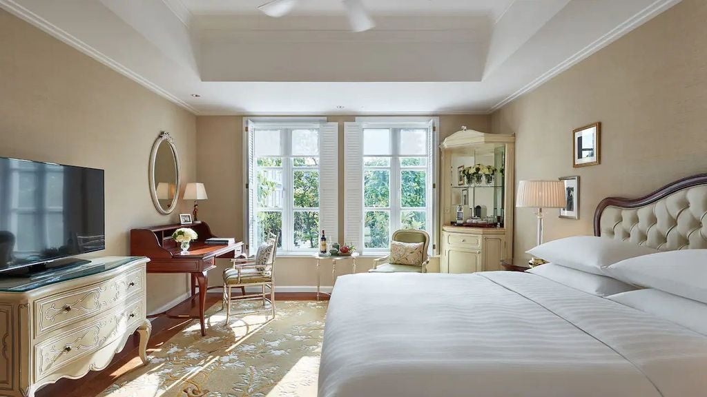 Luxurious king bed with white linens in colonial-style room featuring elegant drapes, classic armchair, and garden-facing windows