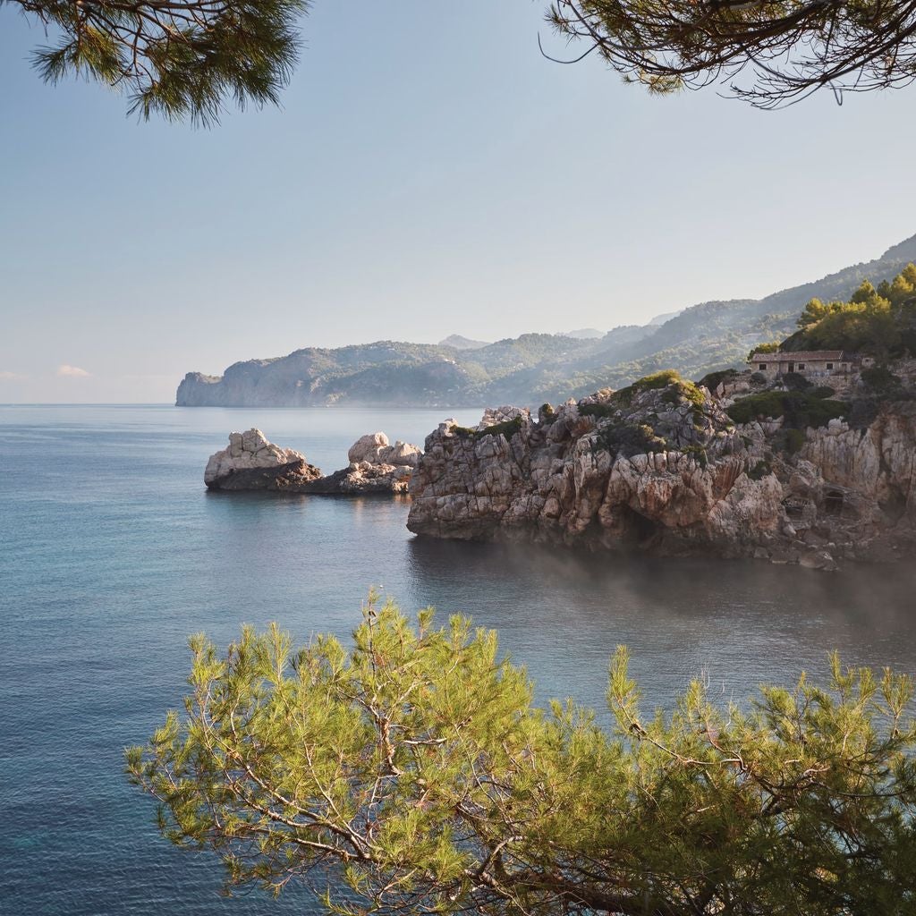 Elegant Spanish villa with stone facade nestled in Mallorca mountains, featuring lush gardens, terracotta roofs and Mediterranean charm