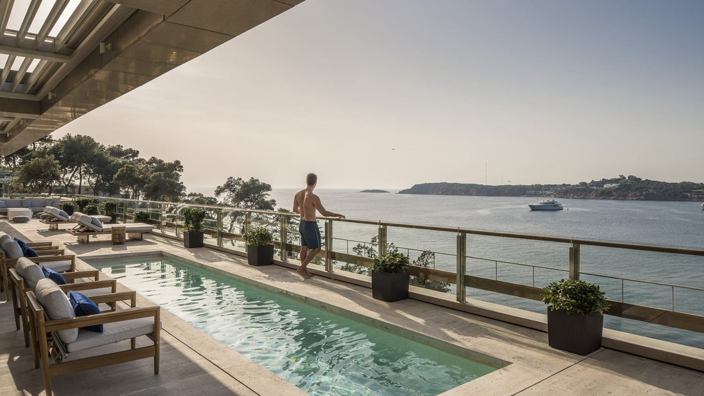 Luxurious coastal suite with floor-to-ceiling windows, modern furnishings, marble bathroom, and panoramic views of the Aegean Sea