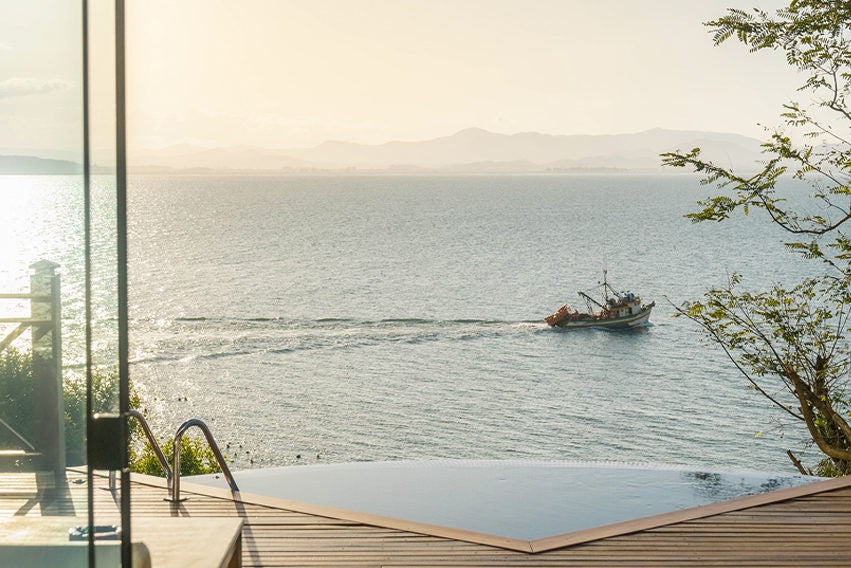 Luxurious overwater bungalow with infinity pool overlooking emerald bay, surrounded by lush Brazilian rainforest at sunset