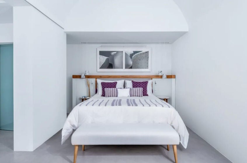 Elegant white-walled suite with private plunge pool overlooking Santorini caldera, featuring minimalist decor and curved archways