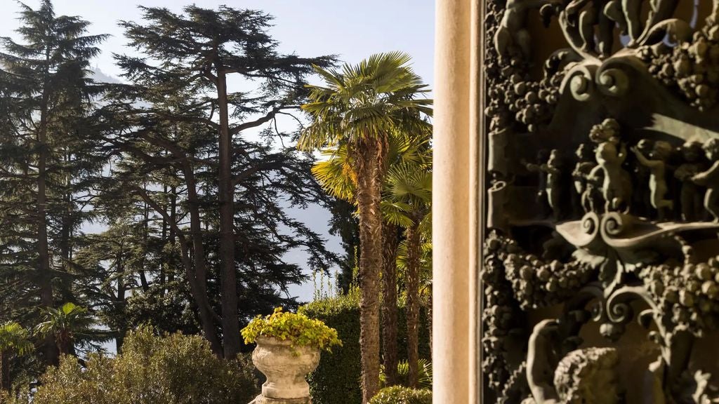 Elegant Italian villa hotel perched on Lake Como's hillside, featuring grand stone terraces, manicured gardens and classic architecture