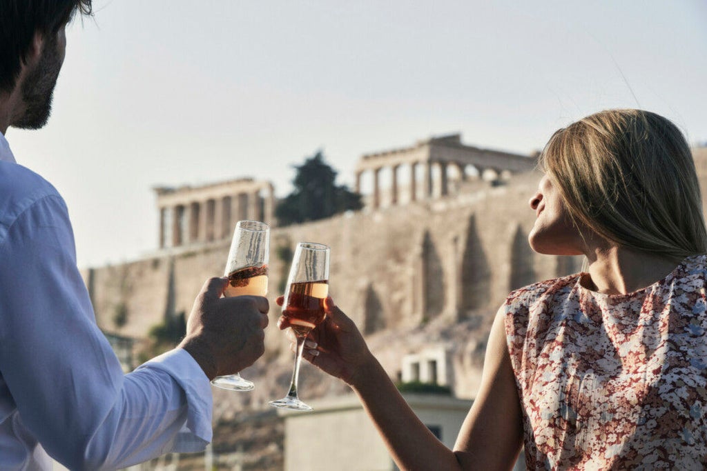 Elegant modern hotel facade with glass balconies and classic Greek columns, set against Athens cityscape at golden hour