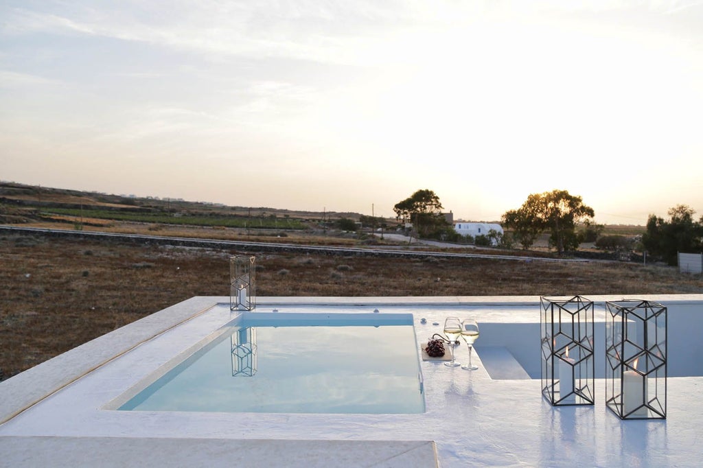 Luxurious white-washed Greek villa nestled on Santorini's cliffside, featuring elegant arched windows, blue-domed roof, and panoramic Aegean Sea view