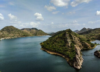 Opulent hotel complex with white domed towers and archways reflected in tranquil lake waters, set against misty mountain landscape