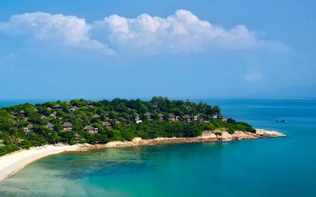 Luxurious infinity pool overlooking the Gulf of Thailand at Six Senses Samui, with wooden deck chairs and lush tropical vegetation