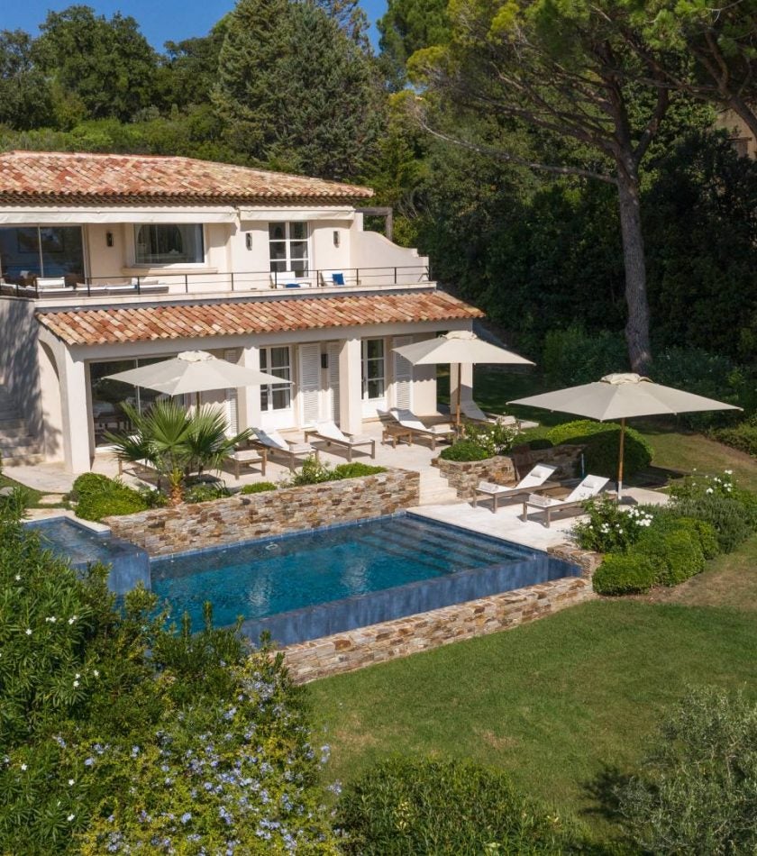 Modern coastal hotel with infinity pool overlooking Mediterranean Sea, surrounded by manicured gardens and elegant white terraces