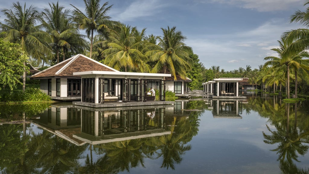 Modern overwater villa with infinity pool overlooking turquoise ocean at dusk, surrounded by tropical gardens and palm trees